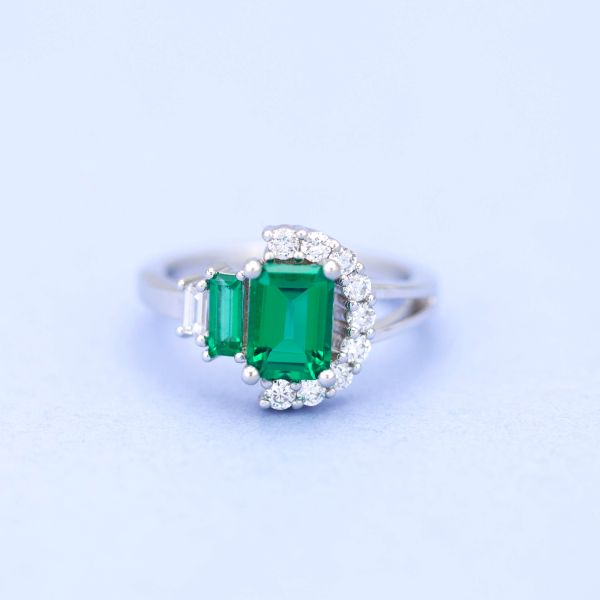 Modern, asymmetrical engagement ring with emerald and a semi-halo of diamonds.