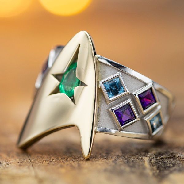 A large Star Trek inspired logo acts as a setting for the pear-cut emerald center stone.