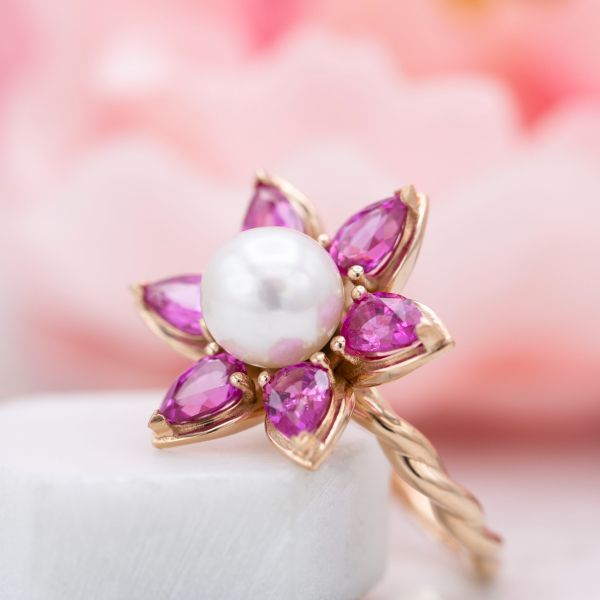 粉红色的蓝宝石花瓣衬托出这枚花戒指珍珠中心宝石的光泽