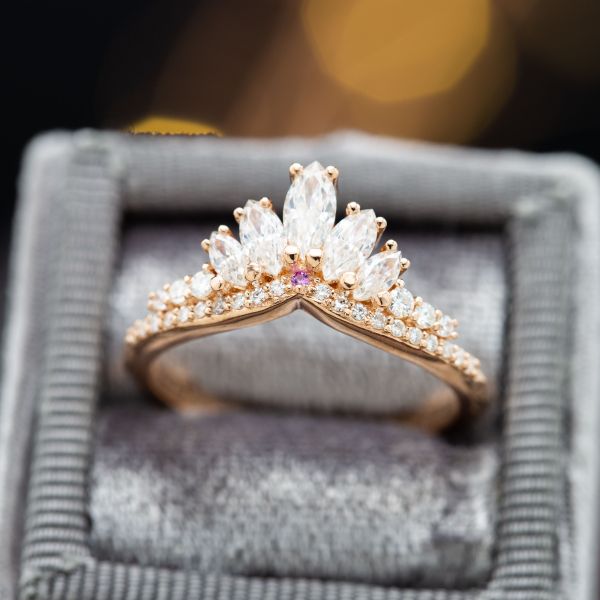 Marquise和圆形切割钻石创造了一个优雅的皇冠灵感曲线与粉红色蓝宝石在中心。