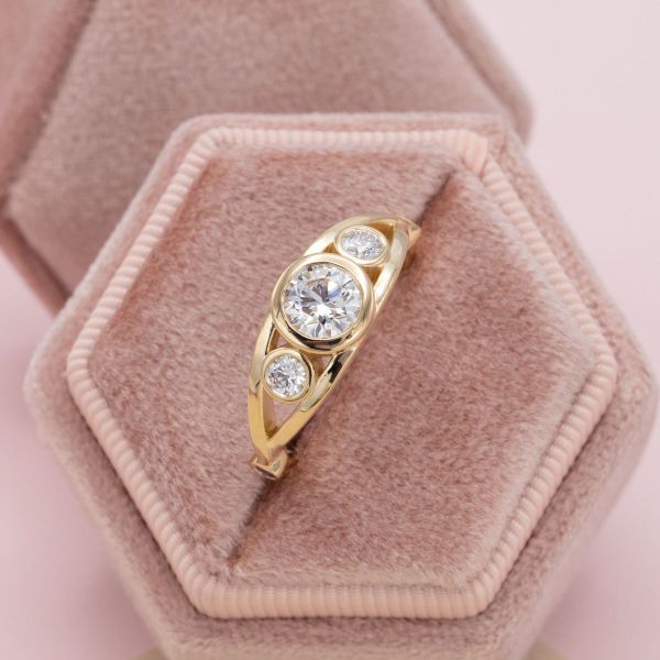 A bezel-set center diamond and diamond side stones sit on a yellow gold band.