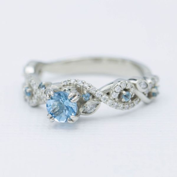 这枚戒指的灵感来自海洋和她对户外的热爱，它围绕着水色调缠绕着精致的波浪状钻石链，中心是一颗清晰的蓝色海蓝宝石。
