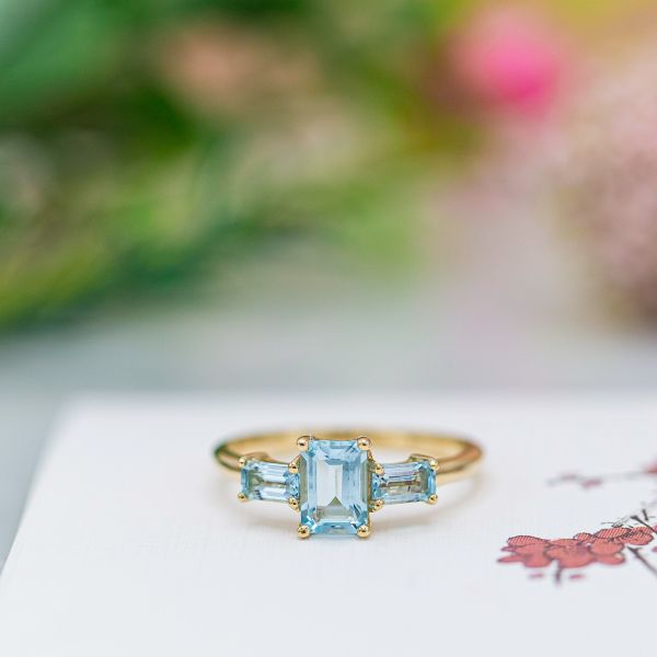 A pair of sky blue topaz side stones help create a three-stone ring on a budget, adding just over $120 to this ring. Similarly sized aquamarines would add closer to $320, while blue sapphires would run closer to $400 for a pair of lab-created stones or anywhere between $700 - $2,000 for a pair of mined stones.