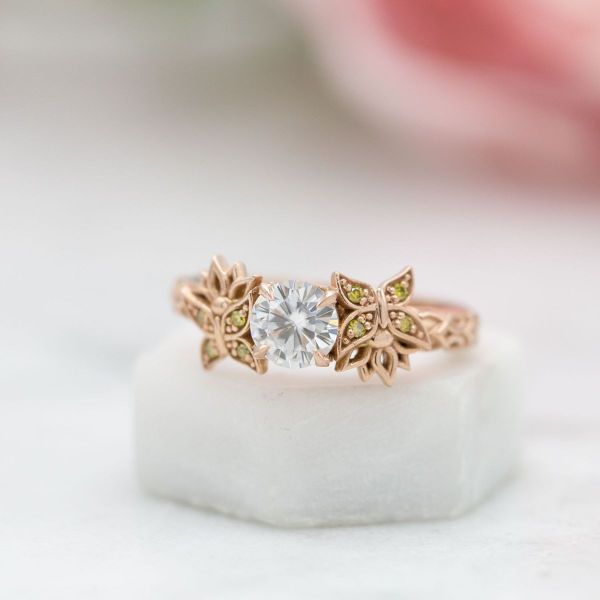 Yellow diamond accented butterflies sit on either side of a moissanite center stone in this one-of-a-kind engagement ring.