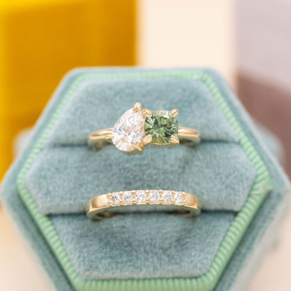 A sweet, asymmetrical toi-et-moi setting of diamond and green sapphire pairs with a straight, sparkling wedding band.