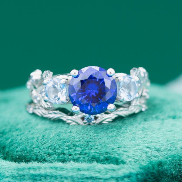 Something old, something new, something borrowed, and something blue! Both "new" and "blue" are covered in this platinum bridal set featuring a lab-created blue sapphire center stone with aquamarine accents. Leafy sculptures make up both bands, reaching towards the ocean blue stone as if to pluck it from the sky.