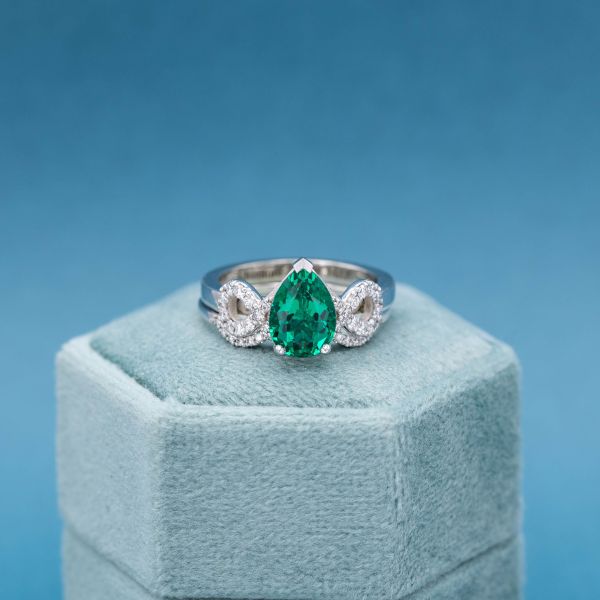 This pear cut emerald sits in a V-prong of white gold with circles of diamonds on either side.