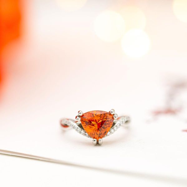The soft curves of a fiery orange sapphire center stone are echoed by the delicate curves of this engagement ring's diamond-lined band.