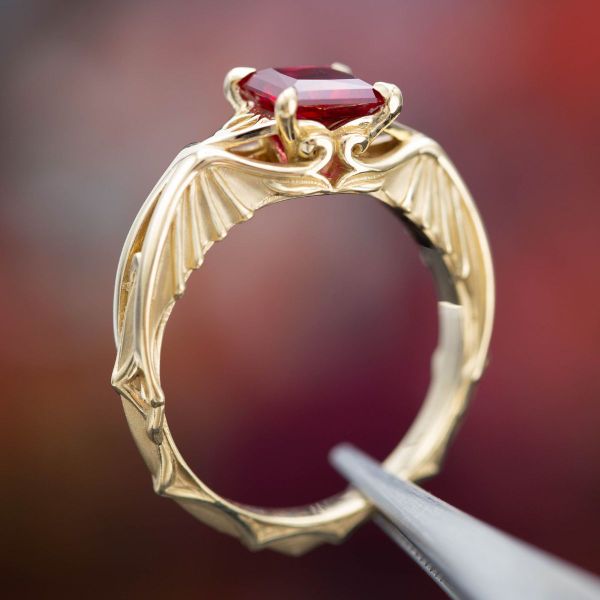Centered by a princess cut ruby, this yellow gold engagement ring features nods to Game of Thrones and Harry Potter.