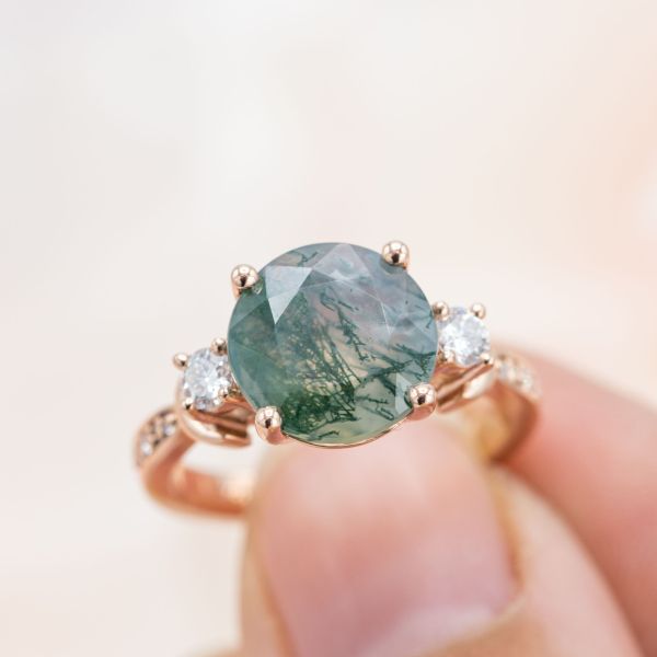 Bold rose gold engagement ring with a vivid moss agate center stone, diamond side stones, and crescent moon details on the band.