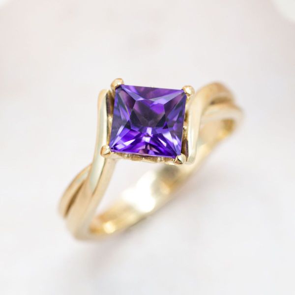 A princess cut amethyst shines a deep purple in this yellow gold engagement ring