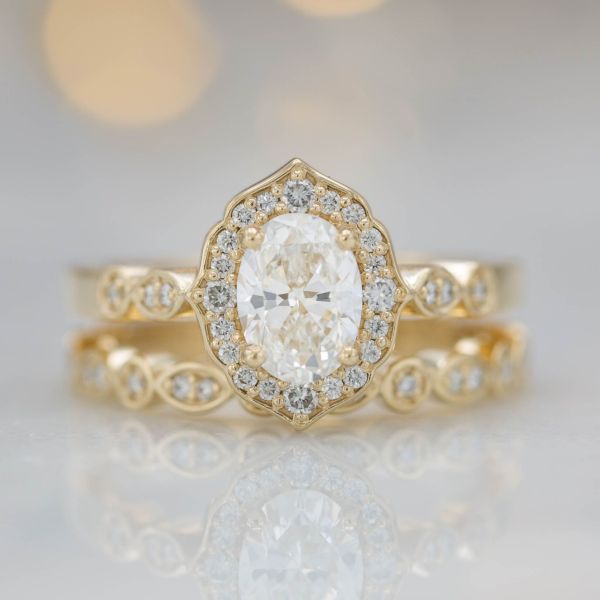 Classic, vintage-inspired floral halo, oval diamond, scalloped shank and matching wedding band.