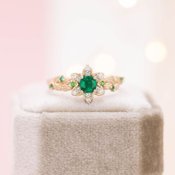 This flower inspired engagement ring features yellow gold, diamonds, and an emerald center stone.