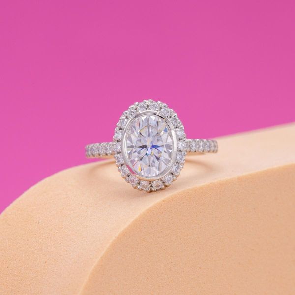 An oval moissanite sits in the center of a moissanite halo and pave band.