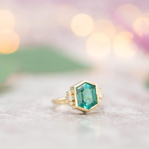 A blue-green hexagonal tourmaline engagement ring in a sleek gold bezel setting.