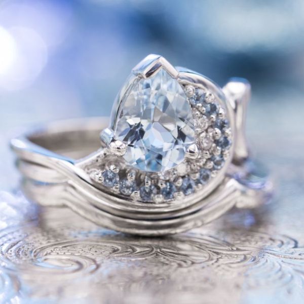 Personal elements in this design: the numbers 5 and 11 (significant dates), the color blue, water (reflective of life on the shores of Lake Superior), modern styling. The bridal set draws all of this together in a wave shape with those exact numbers of accent gems around the pear-cut aquamarine center stone.