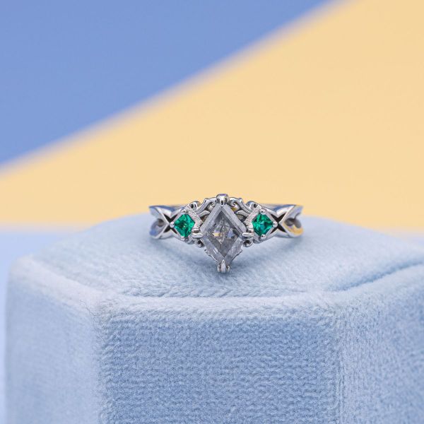 White gold holds a salt and pepper diamond and emeralds in this engagement ring.