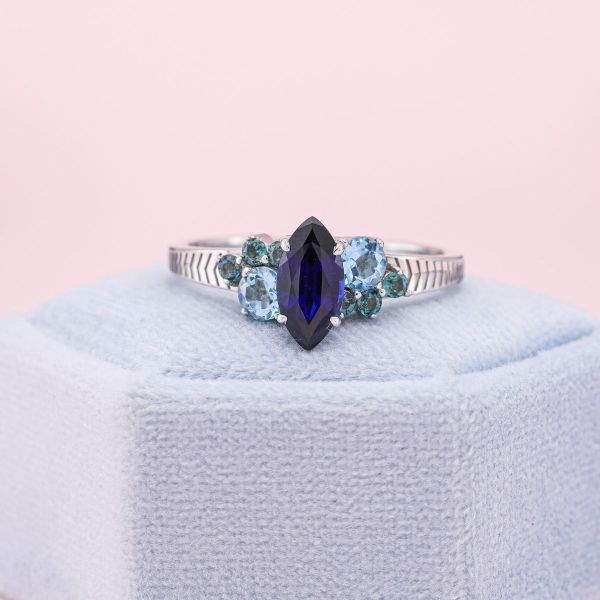 The deep blue of this lab-created sapphire combines beautifully with the light blue topaz and the green-blue alexandrite, bringing to mind the mingling of two seas. The oceanic feel is reflected in the ripple-like motif throughout the yellow gold band.