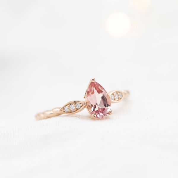 粉红梨形蓝宝石镶嵌在精致的玫瑰金订婚戒指上。