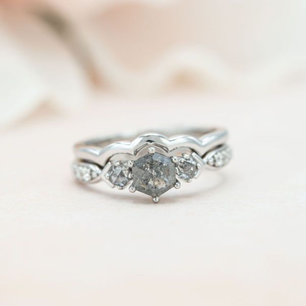 A hexagon cut salt and pepper diamond sits in the center of this three stone white gold engagement ring.