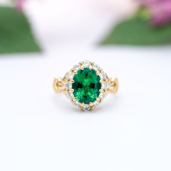 A chubby oval cut emerald sits in a yellow gold engagement ring with a diamond halo.