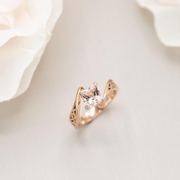 摩根石订婚戒指与公主切割中心石设置在一个角度和玫瑰金带包裹它。