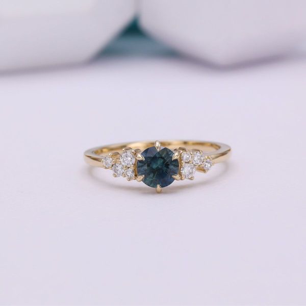 A brilliant round teal sapphire in yellow gold with diamond accents.