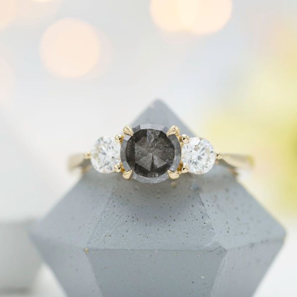 The center salt and pepper diamond is flanked by two white diamonds, all held in a yellow gold setting.