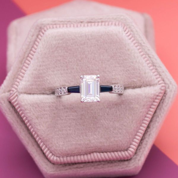 A hidden halo sits just under the emerald cut moissanite center stone in this family inspired engagement ring.