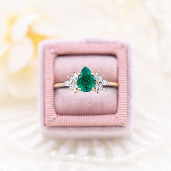 A natural emerald is the centerpiece of this yellow gold engagement ring flanked with marquise cut diamonds.