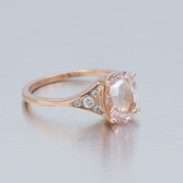 An elegantly curved band opens into an oval morganite center stone, with modern flush settings for the accent diamonds on the ring's shoulders.