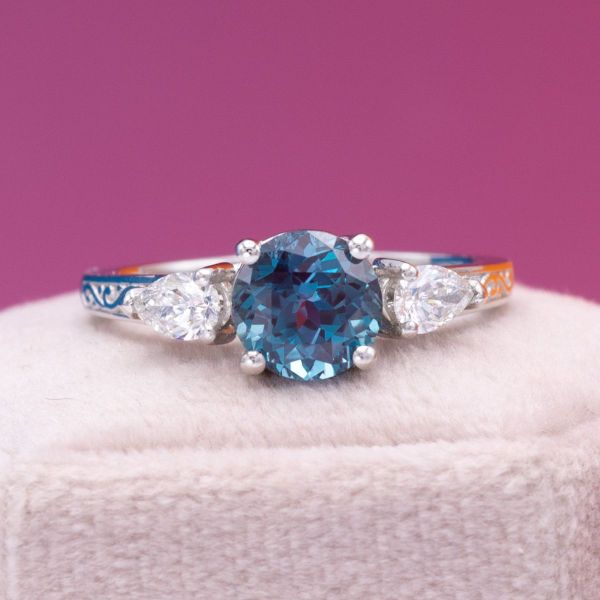 A brilliant round alexandrite sits between two pear cut diamonds in this three stone engagement ring.