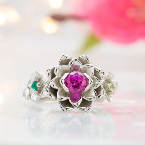 Bold flower ring with a pink sapphire in the lotus blossom and peridot and emerald highlighting the cherry blossom and orchids on the band.
