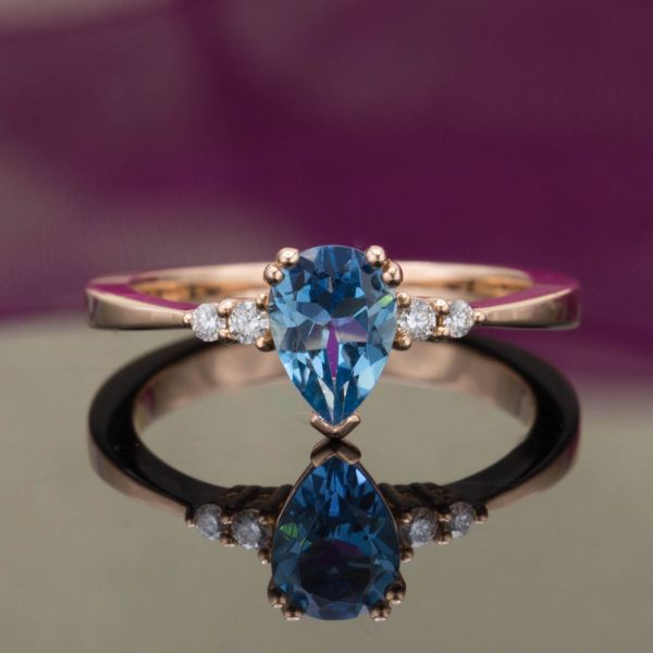 A reverse taper on the rose gold band frames the pear cut aquamarine center stone with diamond accents.