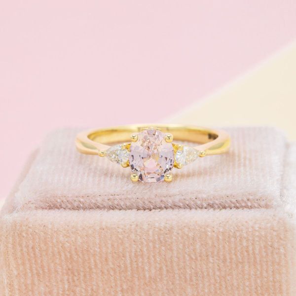 Light pink sapphire engagement ring with diamond accents in yellow gold.