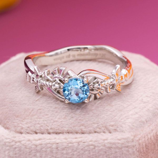Two Master Sword inspired designs flank the Swiss blue topaz center stone in this Zelda inspired engagement ring.