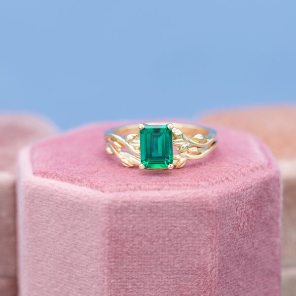 An emerald cut lab created emerald is held by yellow gold vines in a nature inspired engagement ring.