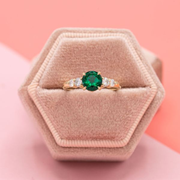 The round brilliant emerald at the center of the yellow gold engagement ring has blue undertones.