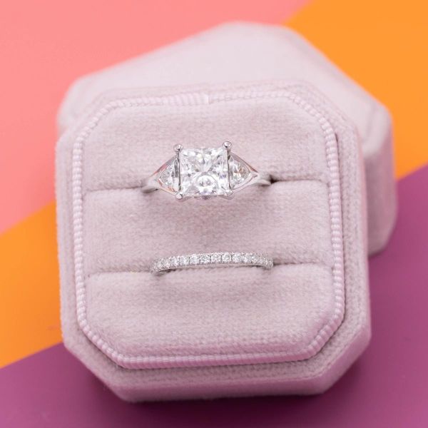 A princess cut moissanite sits in the center of this white gold engagement ring, completed by a matching pave wedding band.
