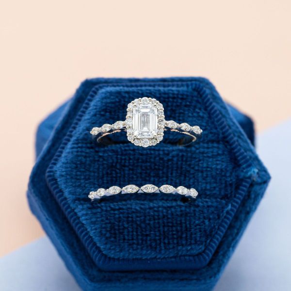 An emerald cut diamond dazzles the eye as it’s surrounded by a halo of diamonds with a modern two-tone setting underneath and a peekaboo sapphire.