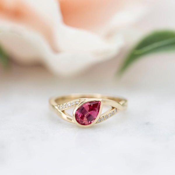 一枚曲线优美的现代订婚戒指，粉色蓝宝石中心镶有一个角度。