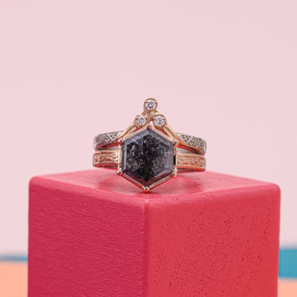 The hexagon cut salt and pepper diamond at the center of this bridal set has mostly black and dark gray with white touches.