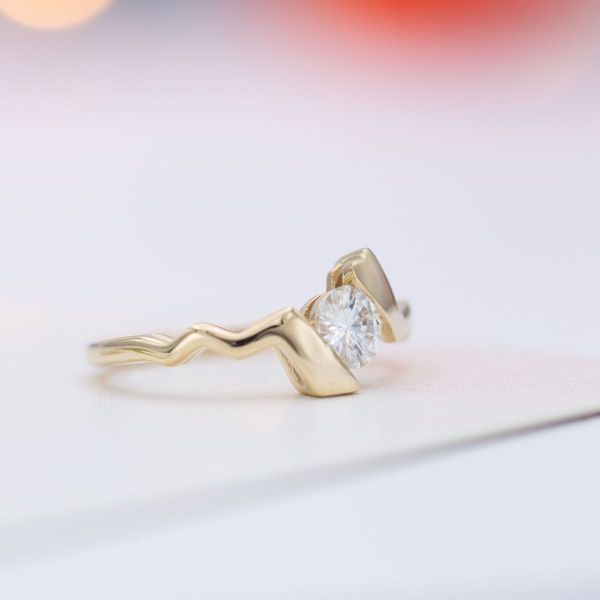 A lightning bolt shaped yellow gold band captures a brilliant round moissanite in the faux tension setting of this Pokémon-inspired engagement ring.
