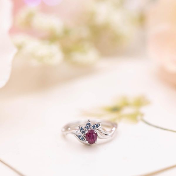 A delicate, floral engagement ring with aquamarine-accented petals partially framing a ruby center stone.