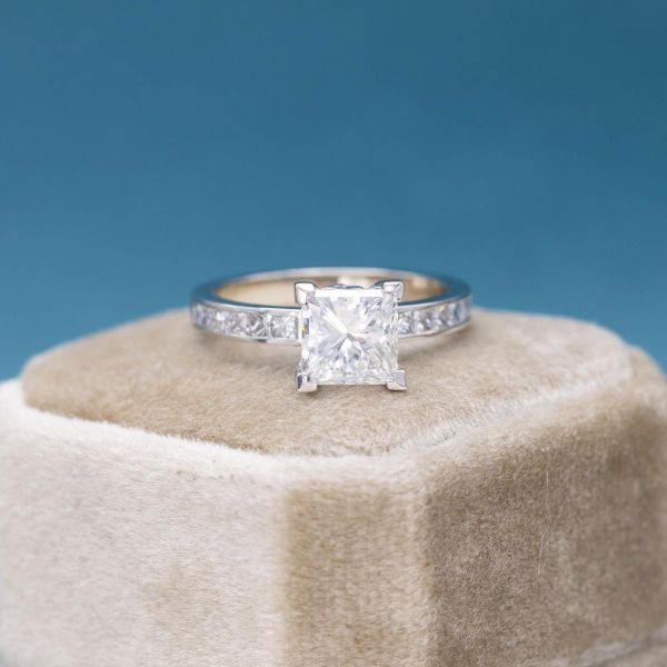 A princess cut, lab created diamond sits in a channel setting of white gold.