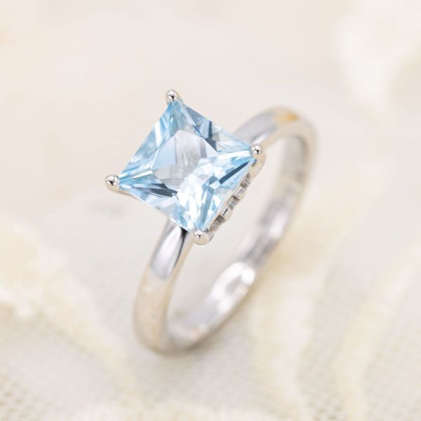 This solitaire engagement ring sports a princess cut blue topaz at its center