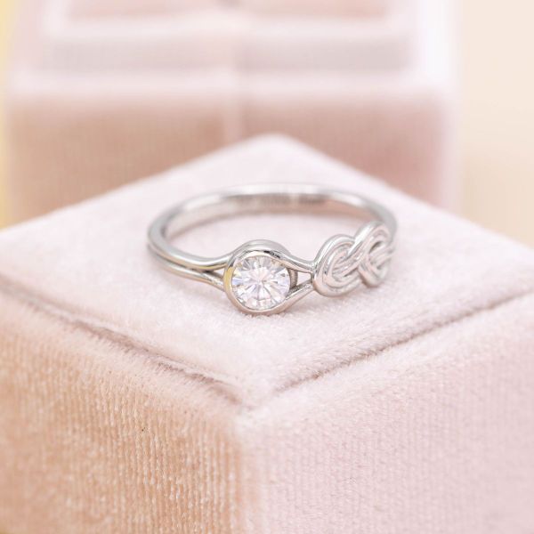 A ring designed for climbing enthusiasts, this setting has a moissanite at the center of a white gold band with a figure 8 knot to the right of the stone.