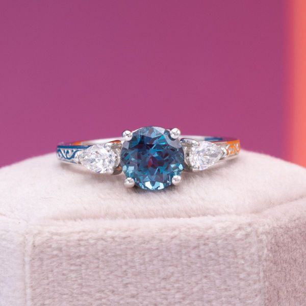 The round cut alexandrite at the center of this engagement ring is a bright teal blue.