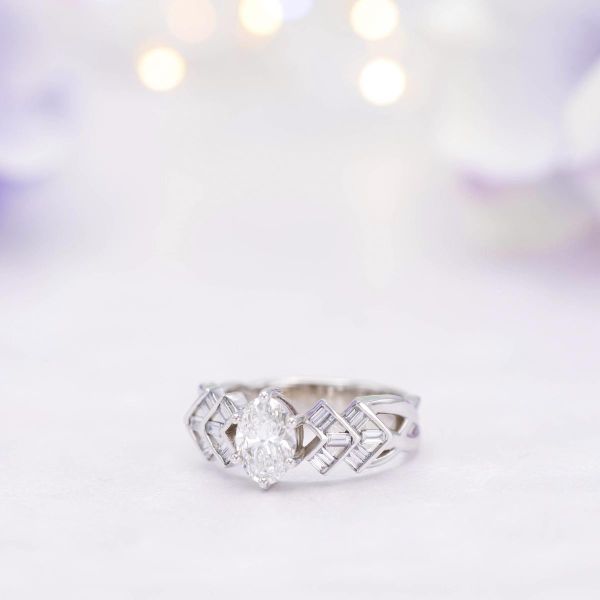 这枚装饰艺术风格的订婚戒指围绕着钻石中心的钻石，上面有v形纹路，镶有长棍钻石。