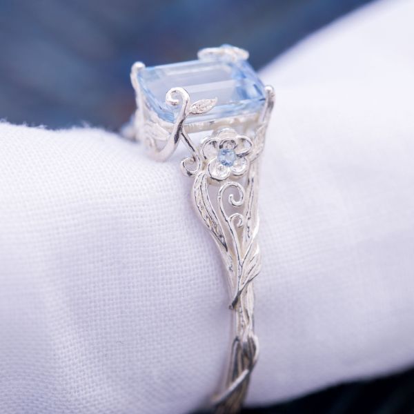 An ethereal, delicate design with vines and flowers surrounding an emerald cut aquamarine center stone.